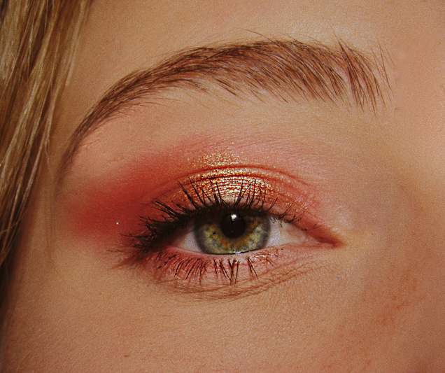 Close-up of hands using a reusable eye makeup stencil on bare eyelid, with soft natural lighting and minimal aesthetic background